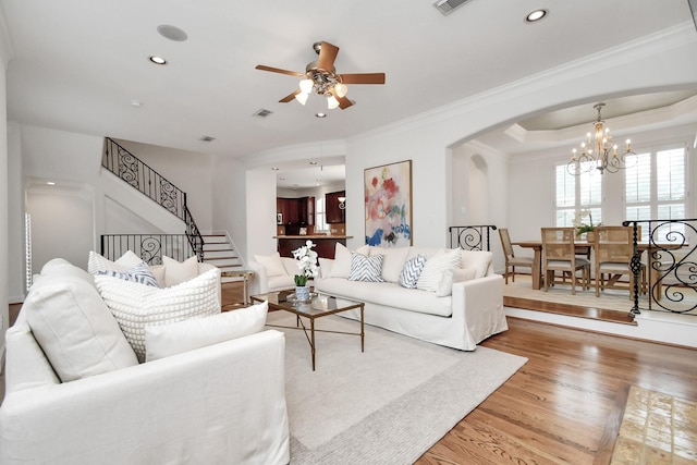 living room with crown molding, ceiling fan with notable chandelier, hardwood / wood-style floors, and a tray ceiling