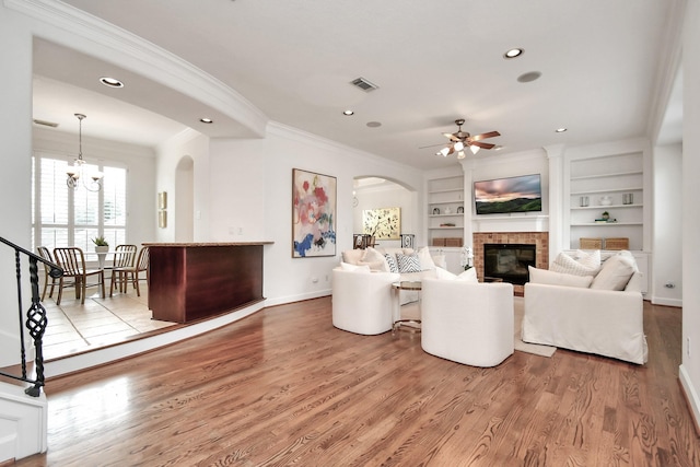 living room with crown molding, wood-type flooring, a fireplace, and built in features