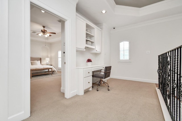 home office featuring built in desk, ornamental molding, ceiling fan, a tray ceiling, and light carpet