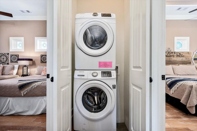 clothes washing area featuring stacked washer / dryer, crown molding, and light hardwood / wood-style floors