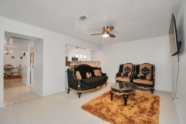 living area featuring ceiling fan with notable chandelier and a textured ceiling