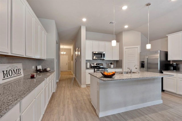 kitchen featuring pendant lighting, light stone counters, white cabinets, and appliances with stainless steel finishes