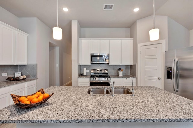 kitchen with hanging light fixtures, stainless steel appliances, white cabinets, and a center island with sink