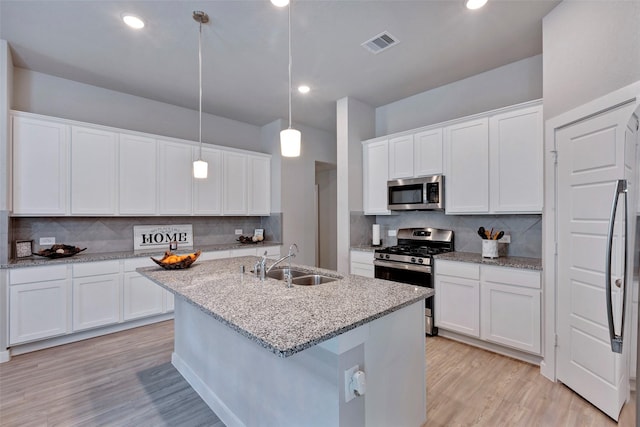 kitchen with appliances with stainless steel finishes, an island with sink, sink, white cabinets, and hanging light fixtures