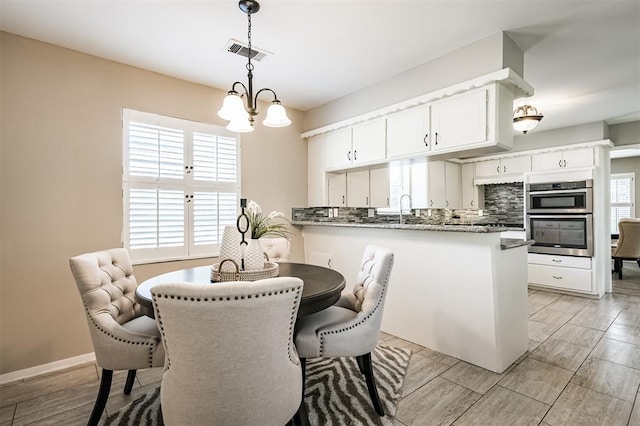 interior space featuring double oven, tasteful backsplash, white cabinetry, dark stone counters, and kitchen peninsula