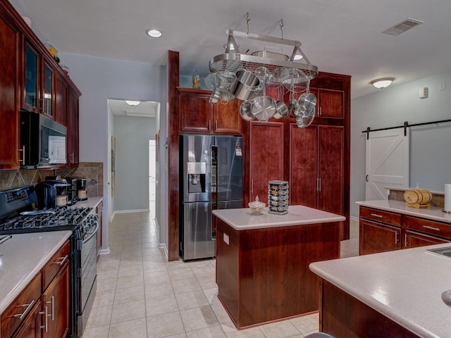 kitchen with stainless steel refrigerator with ice dispenser, light tile patterned flooring, black gas range oven, a kitchen island, and a barn door