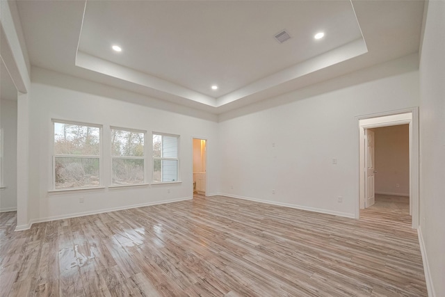 empty room featuring a tray ceiling and light hardwood / wood-style flooring