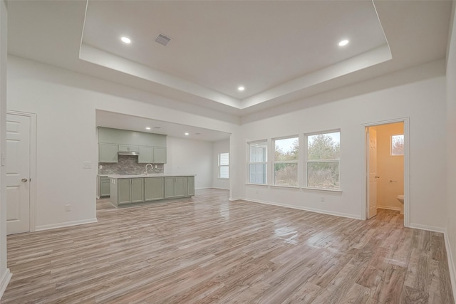 unfurnished living room with sink, a tray ceiling, and light wood-type flooring