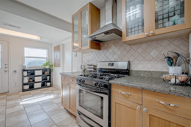 kitchen featuring wall chimney range hood, light tile patterned floors, tasteful backsplash, gas range, and dark stone counters