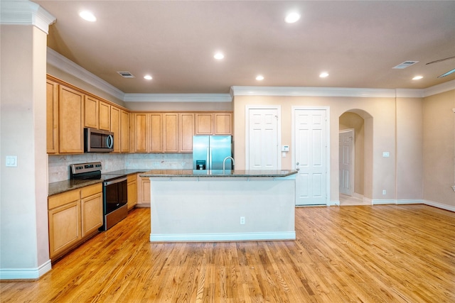 kitchen with tasteful backsplash, stainless steel appliances, an island with sink, and light wood-type flooring