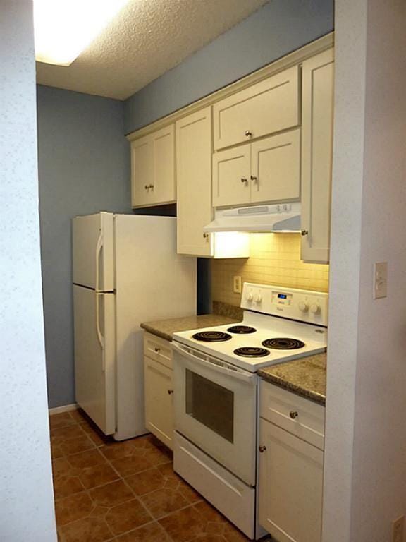 kitchen with tasteful backsplash, dark tile patterned floors, white appliances, cream cabinets, and a textured ceiling