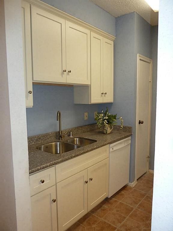 kitchen with light tile patterned flooring, sink, a textured ceiling, dishwasher, and cream cabinets