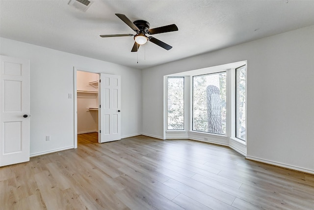 unfurnished bedroom with light hardwood / wood-style flooring, ceiling fan, a textured ceiling, a walk in closet, and a closet