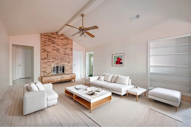 living room featuring vaulted ceiling with beams, light hardwood / wood-style flooring, a brick fireplace, and ceiling fan