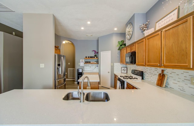 kitchen with sink, tasteful backsplash, range with gas stovetop, stainless steel fridge with ice dispenser, and kitchen peninsula