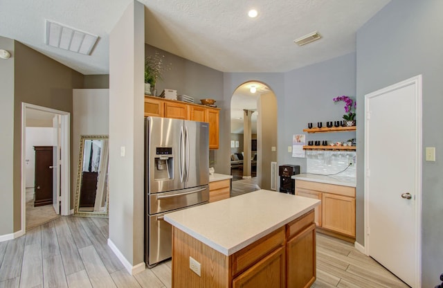 kitchen featuring light hardwood / wood-style flooring, stainless steel fridge, a textured ceiling, and a kitchen island