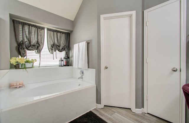 bathroom featuring a tub to relax in, wood-type flooring, and vaulted ceiling