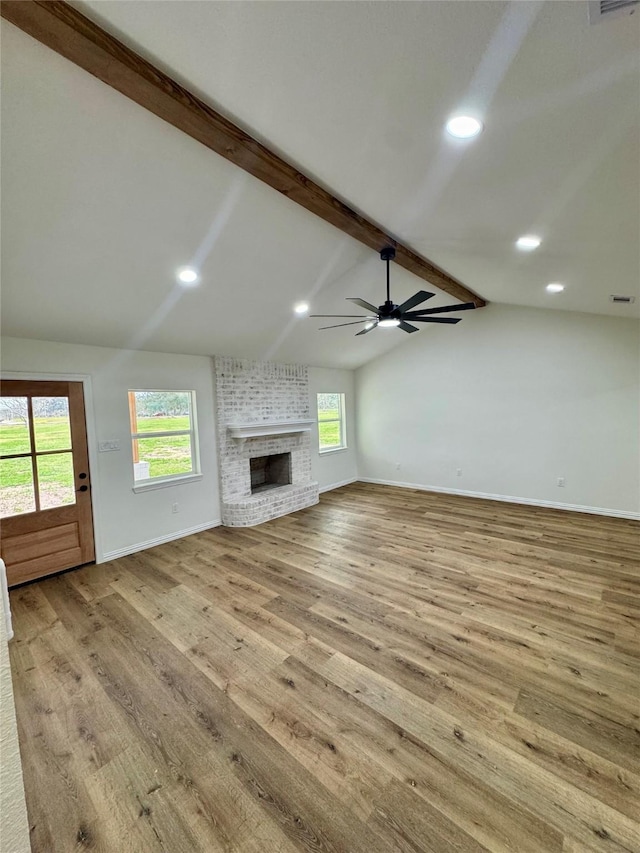 unfurnished living room featuring a brick fireplace, lofted ceiling with beams, light hardwood / wood-style floors, and a healthy amount of sunlight