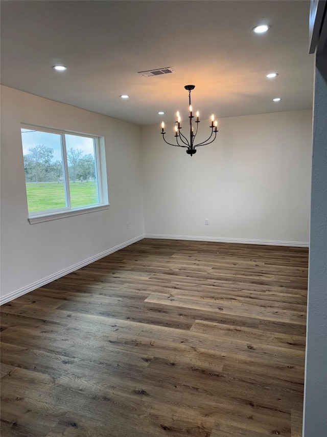 spare room with an inviting chandelier and dark hardwood / wood-style flooring