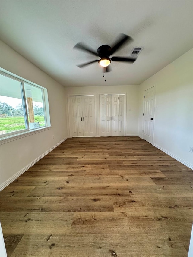 unfurnished bedroom featuring two closets, ceiling fan, and hardwood / wood-style flooring