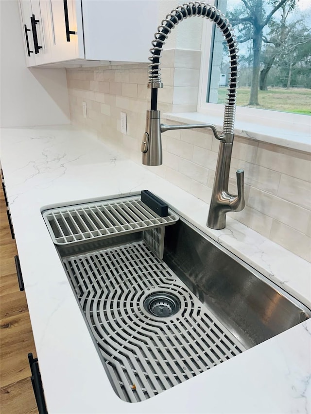 details with white cabinetry, light stone counters, sink, and tasteful backsplash