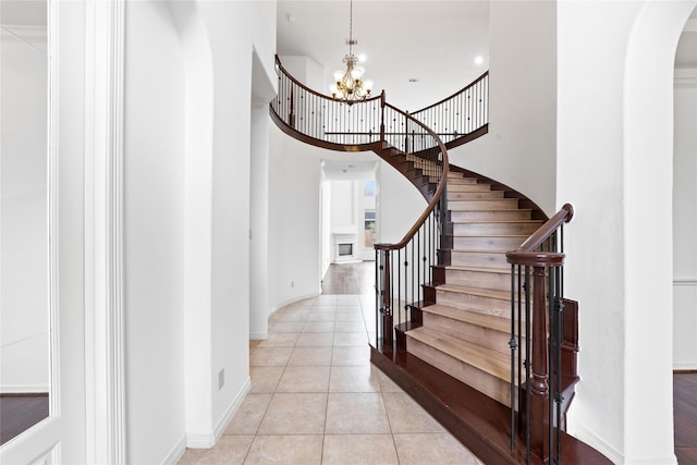 stairway with tile patterned flooring, a towering ceiling, and a notable chandelier