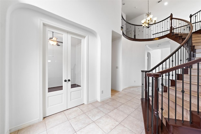 tiled entryway featuring french doors, a towering ceiling, and a chandelier