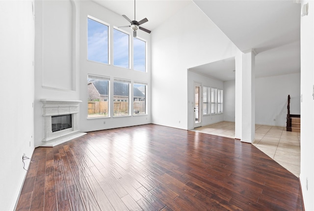 unfurnished living room featuring ceiling fan, light hardwood / wood-style floors, and a towering ceiling