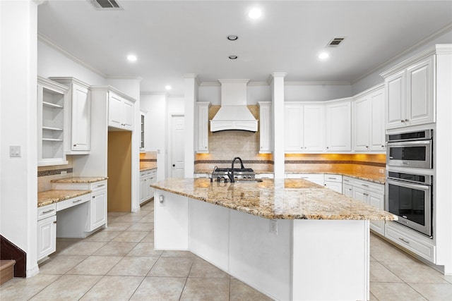 kitchen with light stone countertops, an island with sink, white cabinets, and premium range hood