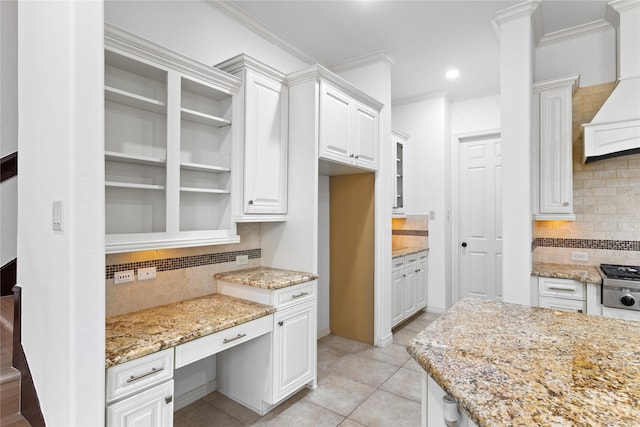 kitchen with custom exhaust hood, white cabinetry, crown molding, light stone counters, and built in desk