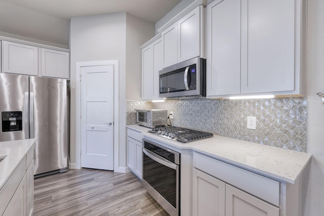 kitchen featuring appliances with stainless steel finishes, light stone countertops, light wood-style floors, white cabinetry, and backsplash