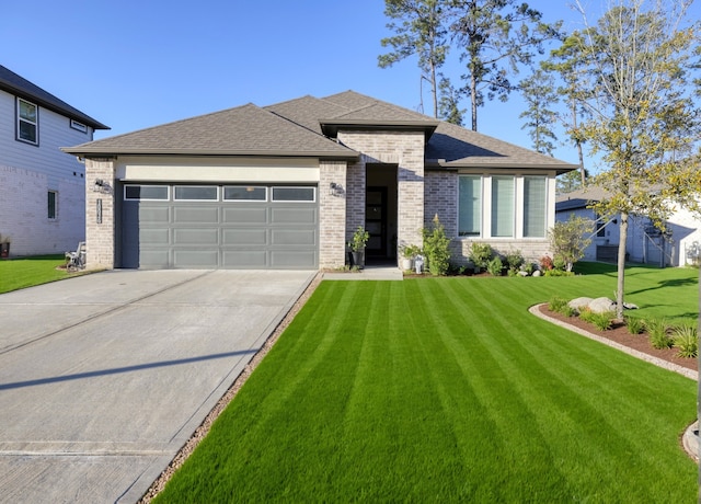 prairie-style house with brick siding, a shingled roof, concrete driveway, a front yard, and a garage