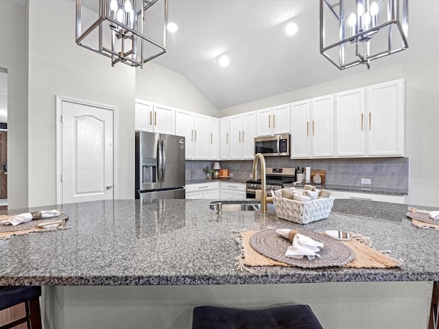 kitchen with a kitchen bar, white cabinetry, dark stone counters, pendant lighting, and stainless steel appliances