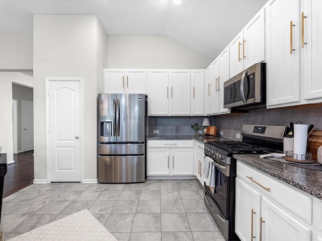 kitchen with white cabinetry, vaulted ceiling, dark stone countertops, stainless steel appliances, and decorative backsplash