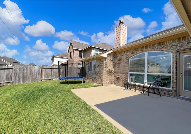 rear view of house featuring a patio, a trampoline, and a lawn