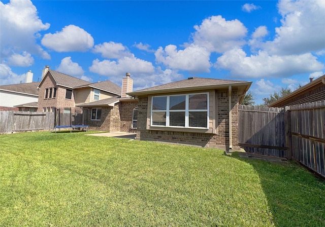 back of property with a trampoline, a yard, and a patio