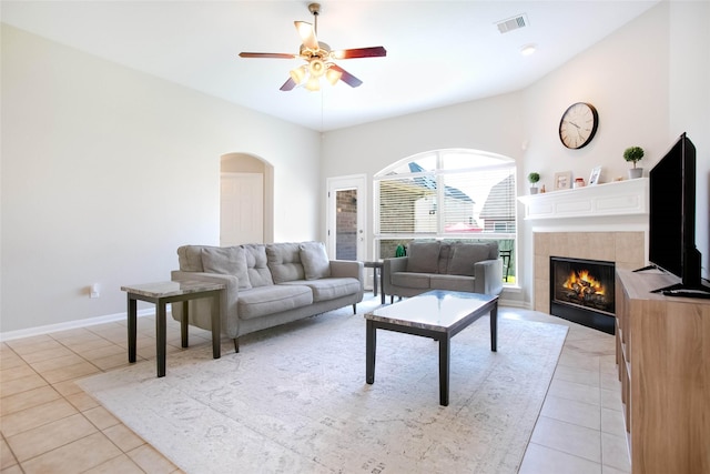 living room with ceiling fan, a tiled fireplace, and light tile patterned floors