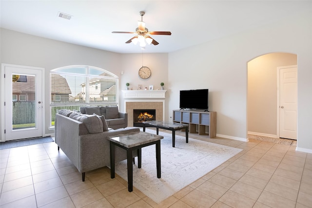 tiled living room with a tile fireplace and ceiling fan