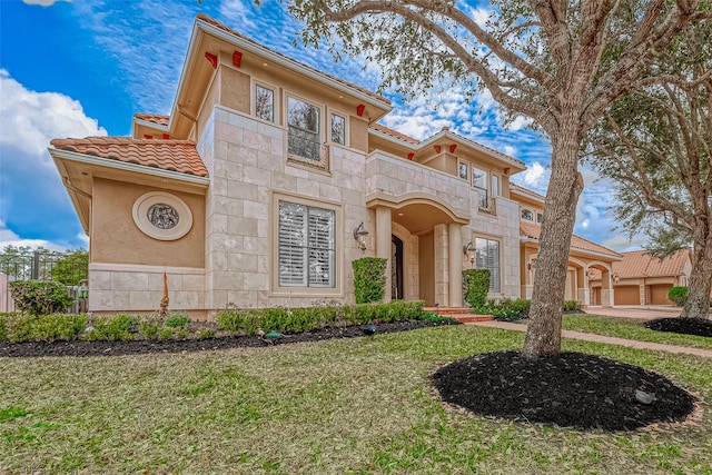 mediterranean / spanish house with a balcony, a tile roof, stone siding, stucco siding, and a front yard