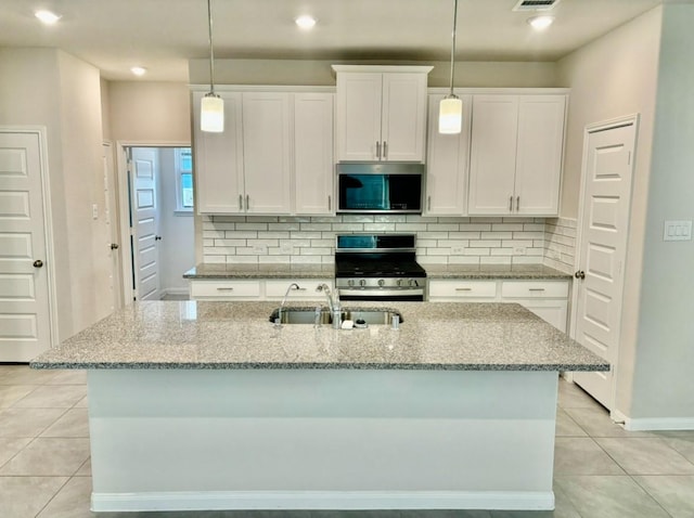 kitchen with appliances with stainless steel finishes, sink, light tile patterned floors, white cabinets, and an island with sink