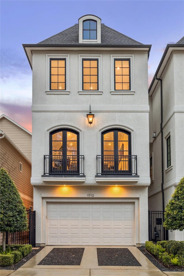 view of front of house with fence, stucco siding, a garage, a balcony, and driveway