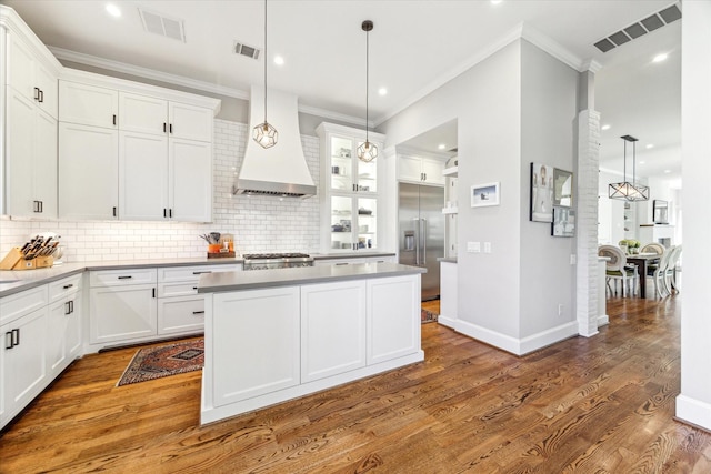 kitchen featuring hanging light fixtures, custom range hood, white cabinets, and stainless steel built in fridge