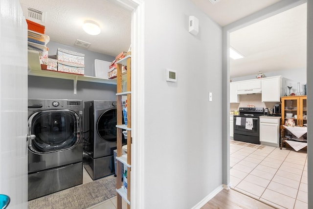 laundry area with light tile patterned floors, washer and clothes dryer, and a textured ceiling