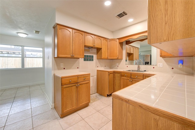 kitchen featuring sink, light tile patterned flooring, decorative backsplash, tile countertops, and kitchen peninsula