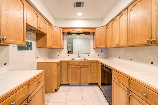 kitchen with sink, light tile patterned floors, tile counters, and black dishwasher