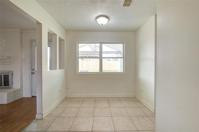 tiled empty room with a brick fireplace and a textured ceiling