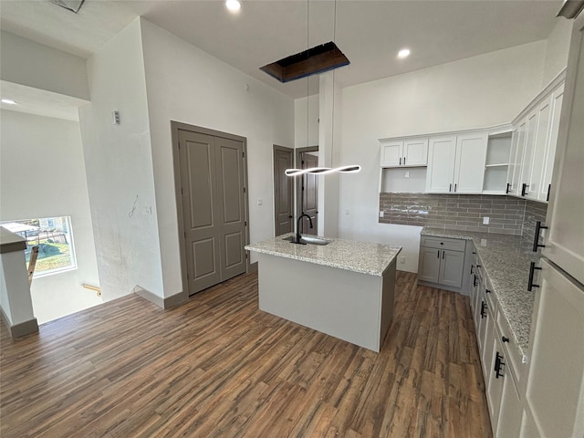 kitchen featuring white cabinetry, light stone counters, dark hardwood / wood-style flooring, and a center island with sink