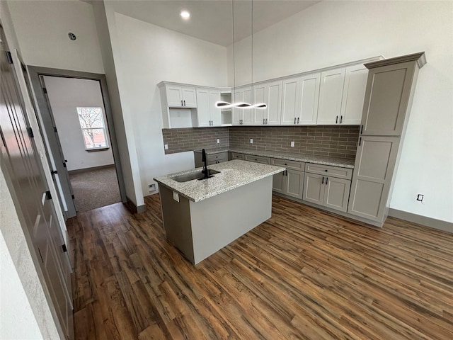 kitchen featuring sink, an island with sink, pendant lighting, a towering ceiling, and light stone countertops