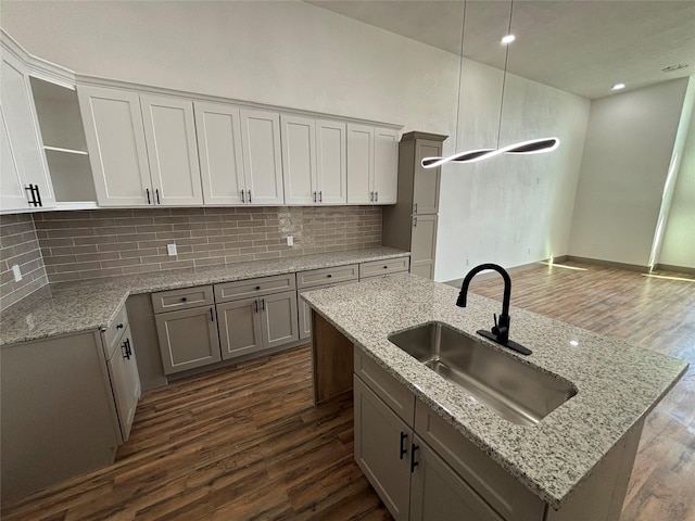 kitchen with an island with sink, sink, dark wood-type flooring, and decorative light fixtures