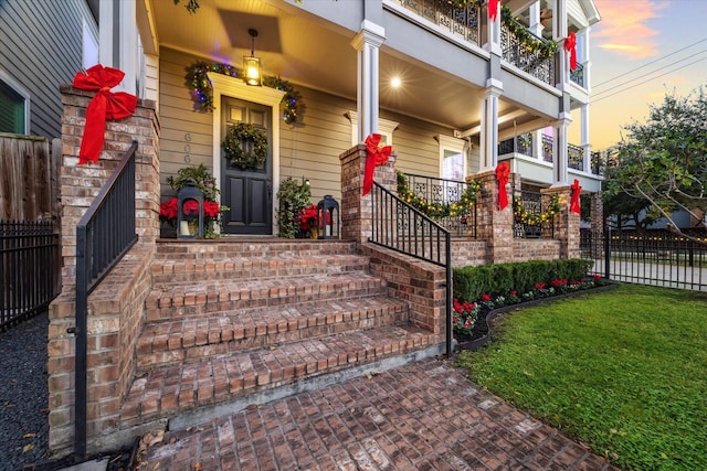 exterior entry at dusk with a yard, a balcony, and covered porch